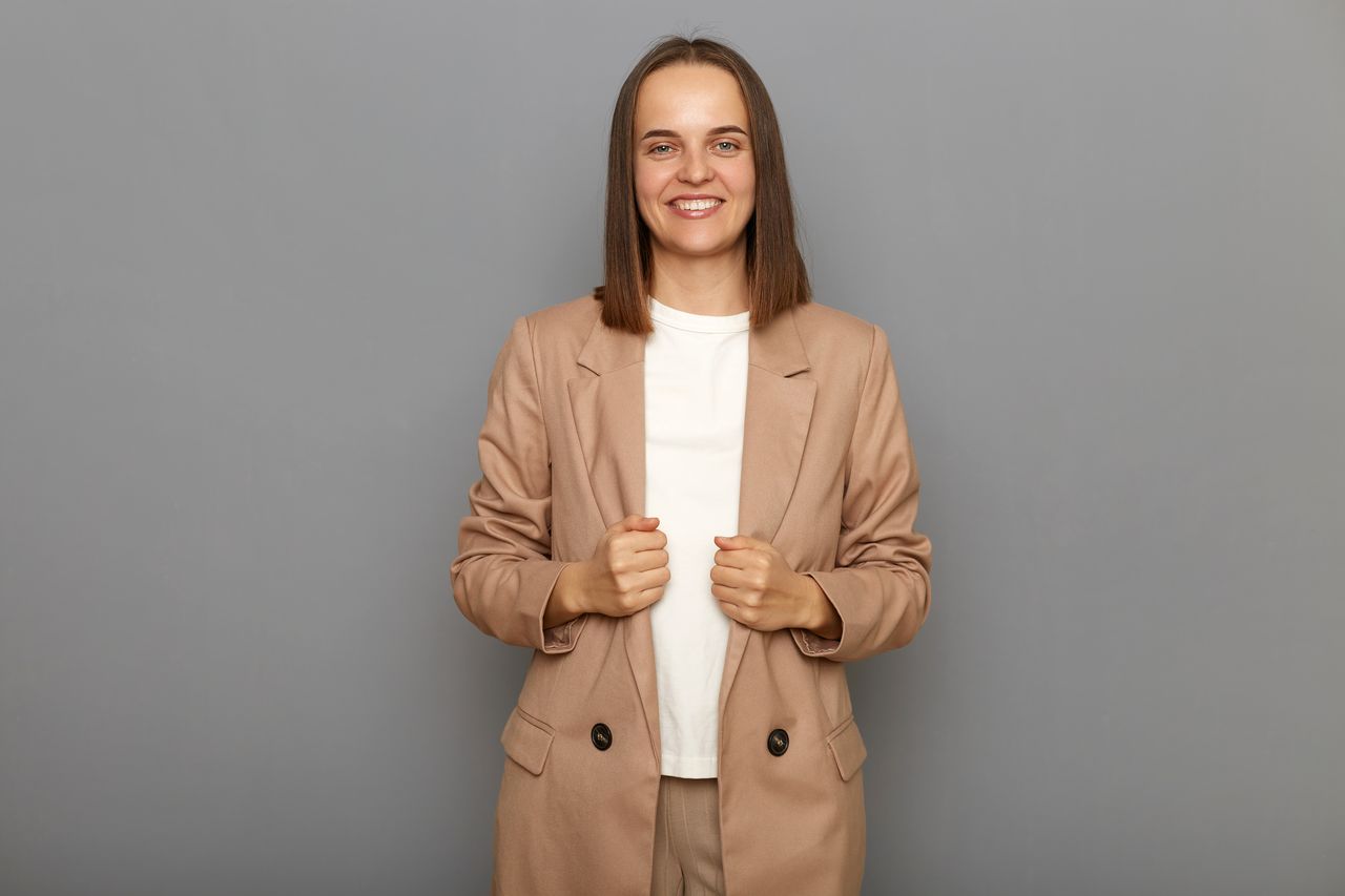 Femme élégante d'une quarantaine d'années, blazer chic, sourire assuré, portrait lumineux dans un intérieur épuré